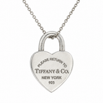 A silver heart-shaped padlock pendant necklace engraved with 'PLEASE RETURN TO TIFFANY & Co. NEW YORK 925', suspended from a delicate silver chain against a plain white background.