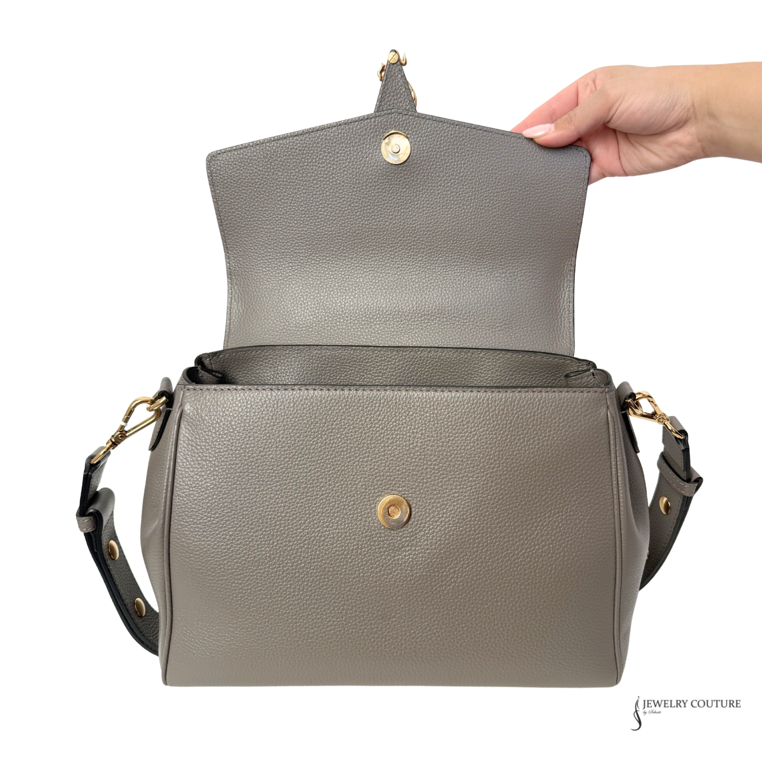 Gray handbag with gold accents held open by a hand on a white background