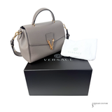 Gray Versace handbag on a black Versace box with a white pouch.
