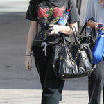 Woman walking on a sidewalk wearing an AC/DC t-shirt and carrying a black Prada  handbag.