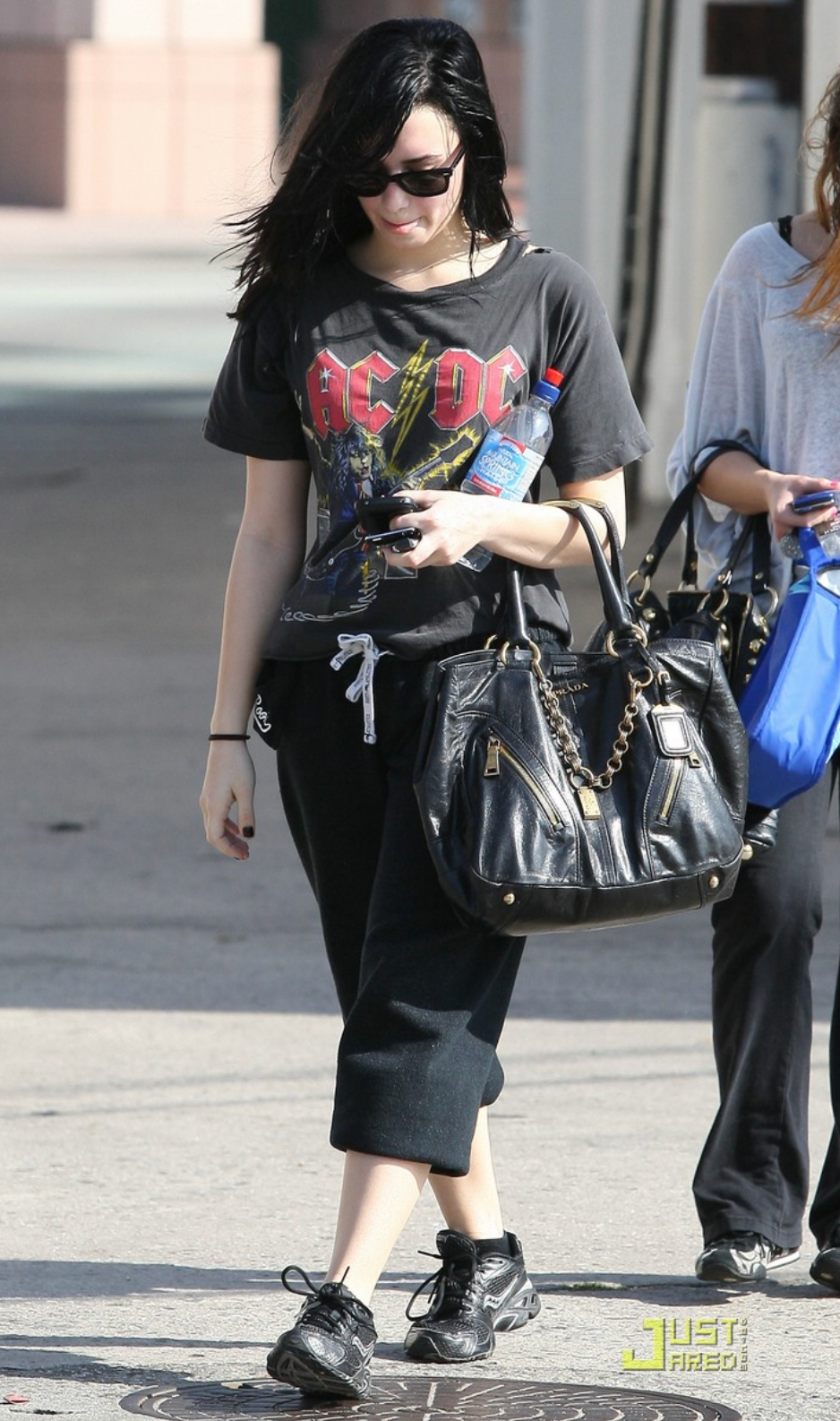 Woman walking on a sidewalk wearing an AC/DC t-shirt and carrying a black Prada  handbag.