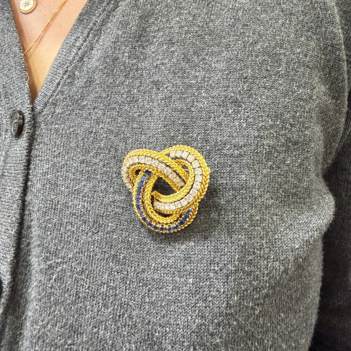 Diamond and sapphire love knot brooch worn on a gray cardigan, close-up