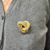 Diamond and sapphire love knot brooch worn on a gray cardigan, close-up