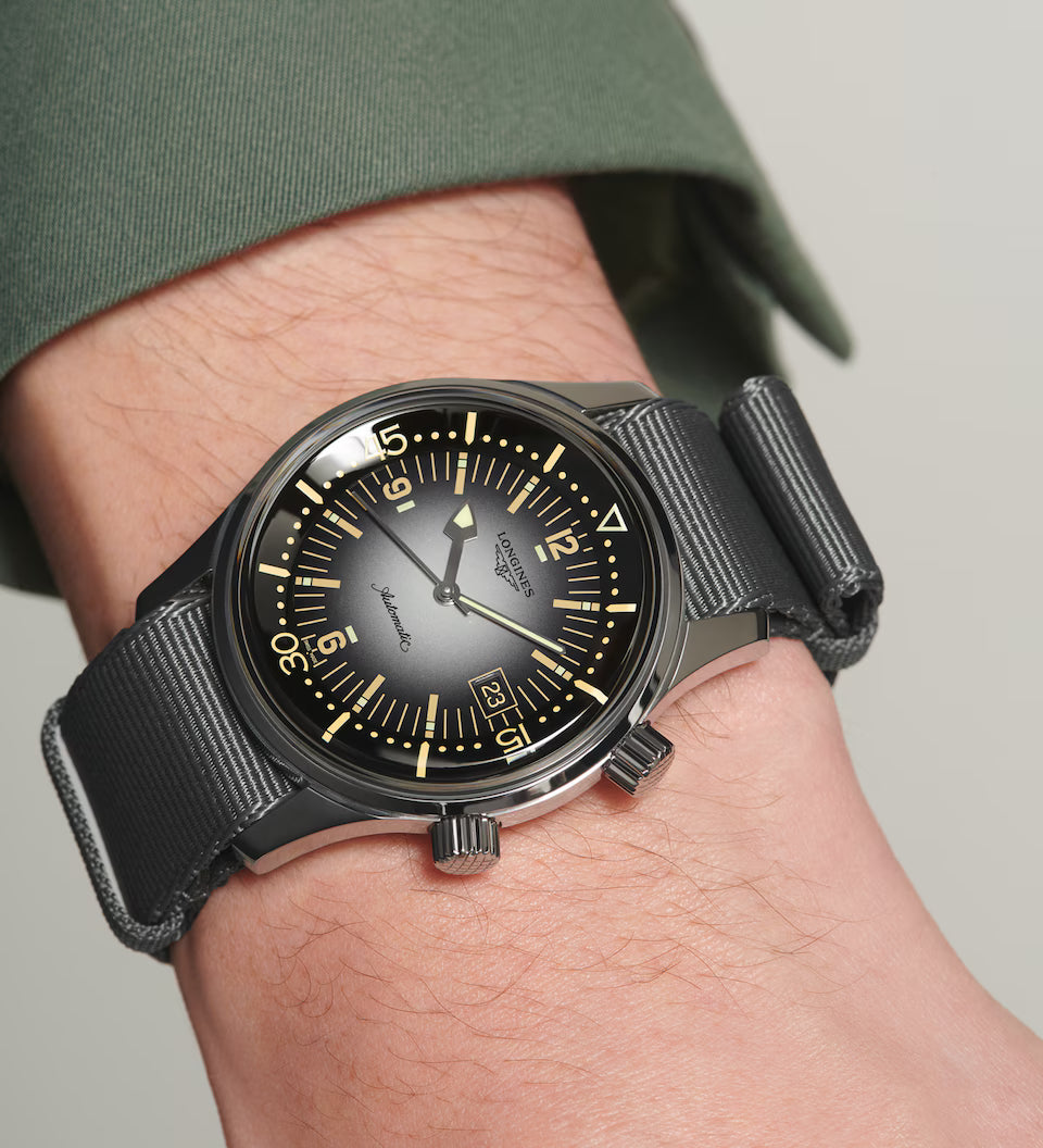 Black wristwatch with a detailed face on a person's wrist against a neutral background