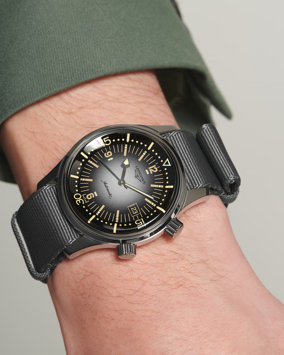 Black wristwatch with a detailed face on a person's wrist against a neutral background