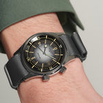 Black wristwatch with a detailed face on a person's wrist against a neutral background