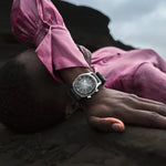 Person wearing a pink shirt and watch, lying on a dark surface with a cloudy sky.