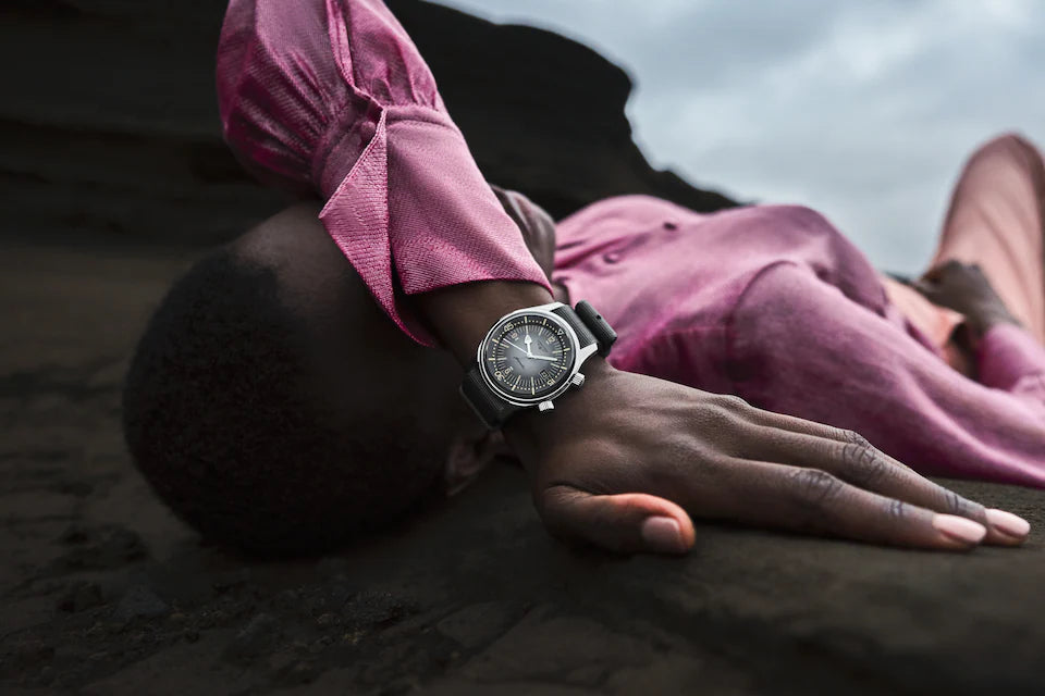 Person wearing a pink shirt and watch, lying on a dark surface with a cloudy sky.