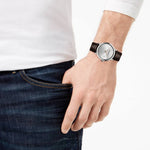 Person wearing a watch with a brown strap on a plain background