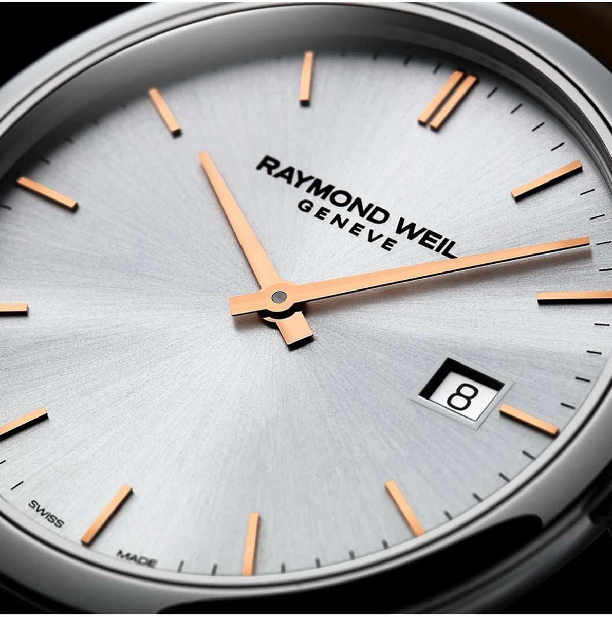 Close-up of a Raymond Weil Geneva watch dial with a silver sunburst finish, rose gold hour markers and hands, and a date window showing the number 8.