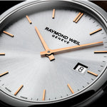 Close-up of a Raymond Weil Geneva watch dial with a silver sunburst finish, rose gold hour markers and hands, and a date window showing the number 8.