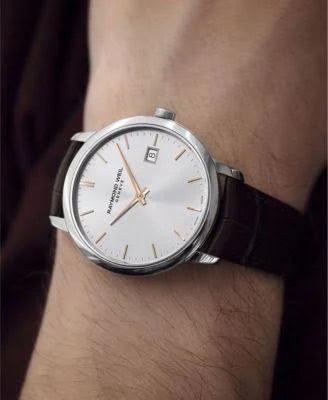 A wristwatch with a silver-toned round case, white dial, and dark brown leather strap worn on a person's wrist.