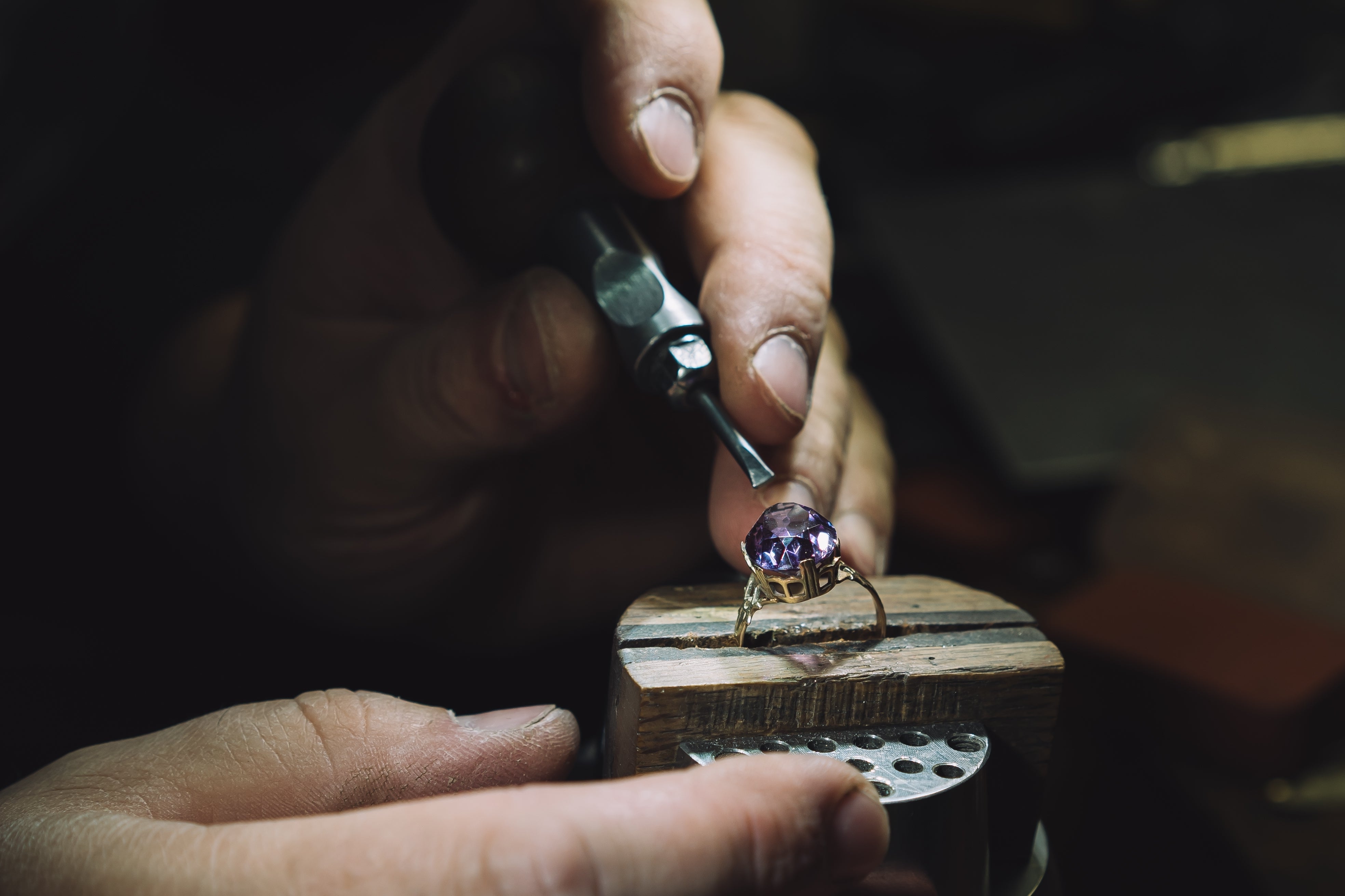 Jeweler working on a ring with a purple gemstone using a tool.