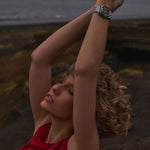 Person with outstretched arms by a body of water, wearing a red top and a watch.